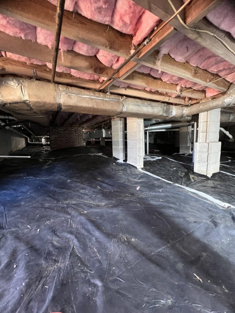 A crawl space with a black vapor barrier installed by Drip Dry Drainage in Cramerton, NC.