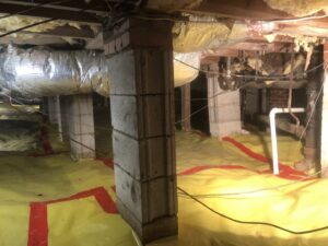 A crawl space with a yellow vapor barrier and concrete block piers, installed by Drip Dry Drainage in Cramerton, NC.