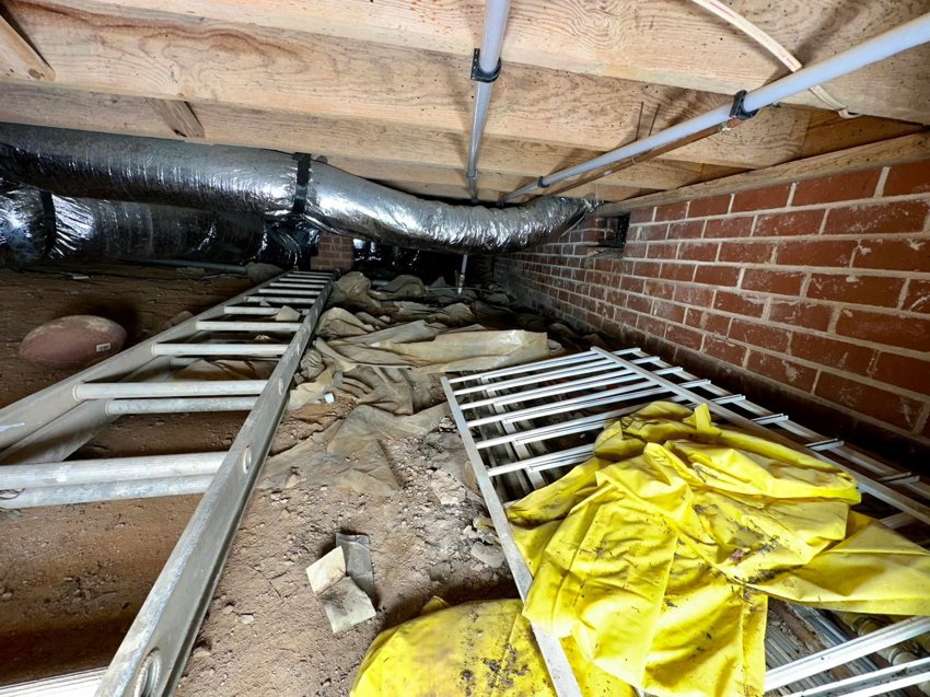 A messy crawlspace with dirt, debris, and a ladder, showing the 'before' state of a waterproofing job by Ramos Waterproofing & Crawlspace Sealing LLC in Durham, NC.