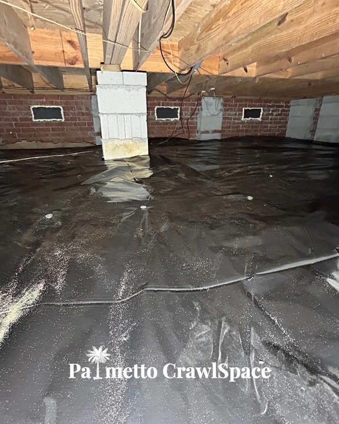 A crawlspace showing a newly installed black vapor barrier by Palmetto Crawlspace, providing moisture control in Mount Pleasant, SC.