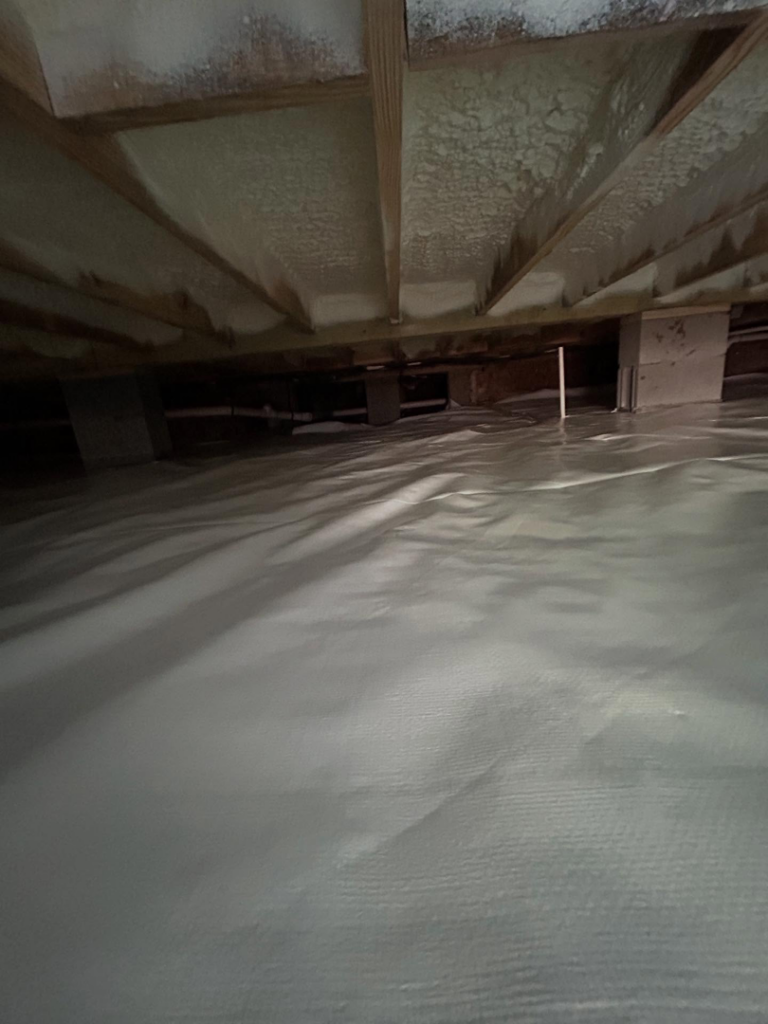 A crawlspace with a new white vapor barrier and spray foam insulation on the subfloor installed by Palmetto Crawlspace in Mount Pleasant, SC.