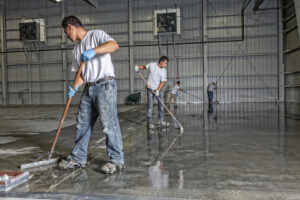 A crew applying an epoxy floor coating in a large warehouse by Alpine Painting and Sandblasting Contractors in Paterson, NJ.