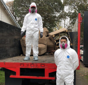 Two crew members in hazmat suits standing on the back of a Great White Junk Removal truck with items to be removed in San Francisco, CA.