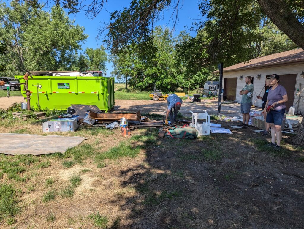 A crew loading various items into a green dumpster from Waste-Away Dumpsters & Disposal LLC during a junk removal job in Sioux Falls, SD.