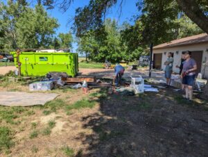 A crew loading various items into a green dumpster from Waste-Away Dumpsters & Disposal LLC during a junk removal job in Sioux Falls, SD.