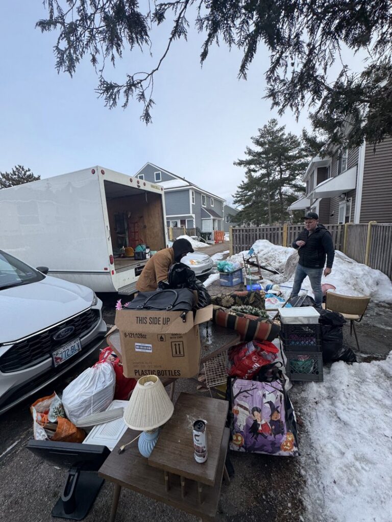 A crew loading various junk items from a snowy driveway into a box truck and trailer for Hometown Hauling 802 in Milton, VT.