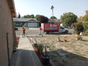 Two crew members loading a metal frame into a Great White Junk Removal truck at a residential property in San Francisco, CA.