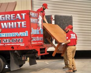 Two crew members loading a wooden table into a Great White Junk Removal truck during a job in San Francisco, CA.