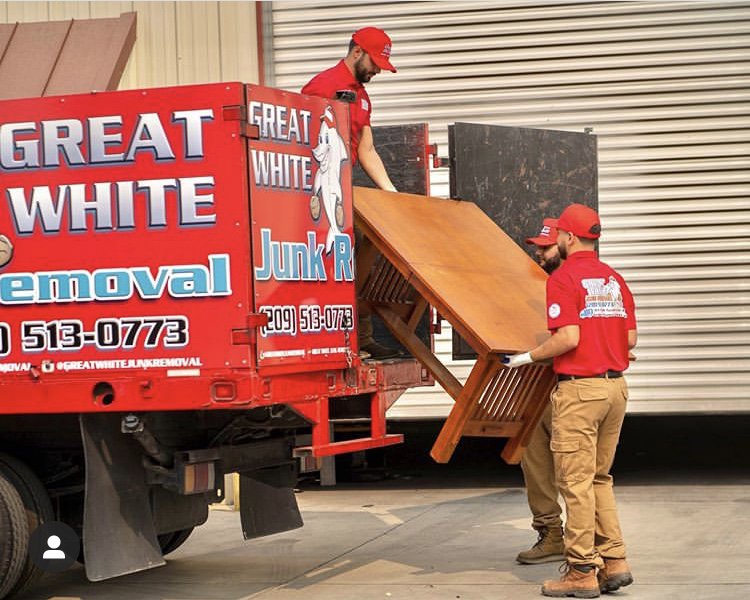 Two crew members loading a wooden table into a Great White Junk Removal truck during a job in San Francisco, CA.