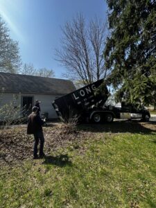 A crew member loading yard waste into a Long Dumpster Rentals dumpster during a general junk removal job in Rochester, NY.