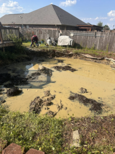 A crew member clearing mud and debris from a drained pool area for Weekly Waste Solutions in Jackson, MS.