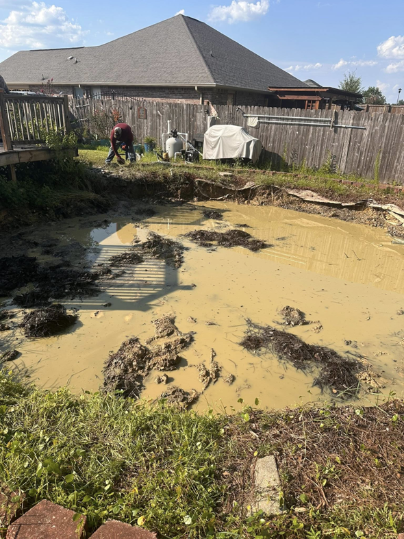 A crew member clearing mud and debris from a drained pool area for Weekly Waste Solutions in Jackson, MS.