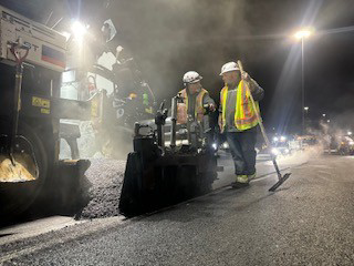A crew operating an asphalt paver to lay new pavement at night for Northeast-Paving in Bangor, ME