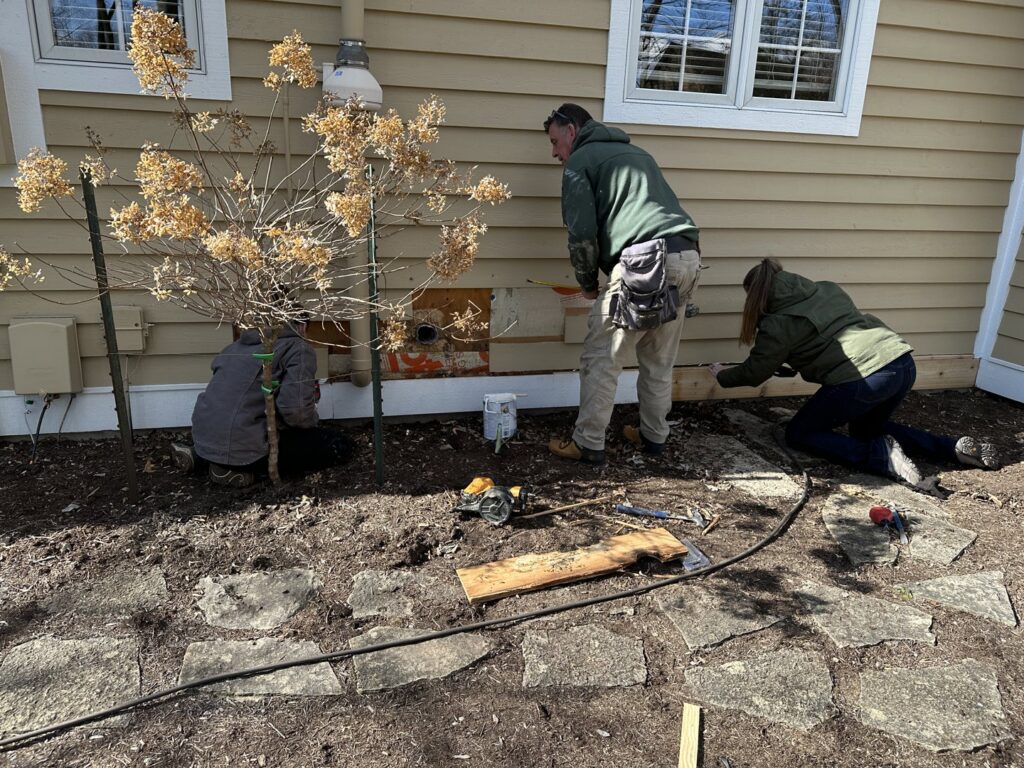 A crew repairing the base of a house's siding with tools on the ground by Cedar Siding Repair in Centerville, OH.
