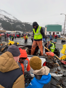 A crew in high-visibility vests sorting and loading debris from a truck bed during a cleanup operation by Alaska Waste in Anchorage, AK.