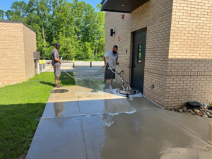 A crew member using a surface cleaner to pressure wash a concrete sidewalk for Selk Solutions in Crossville, TN.