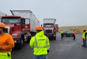 A crew in safety gear with Voyager Trucking waste hauling trucks at a job site in Newark, NJ