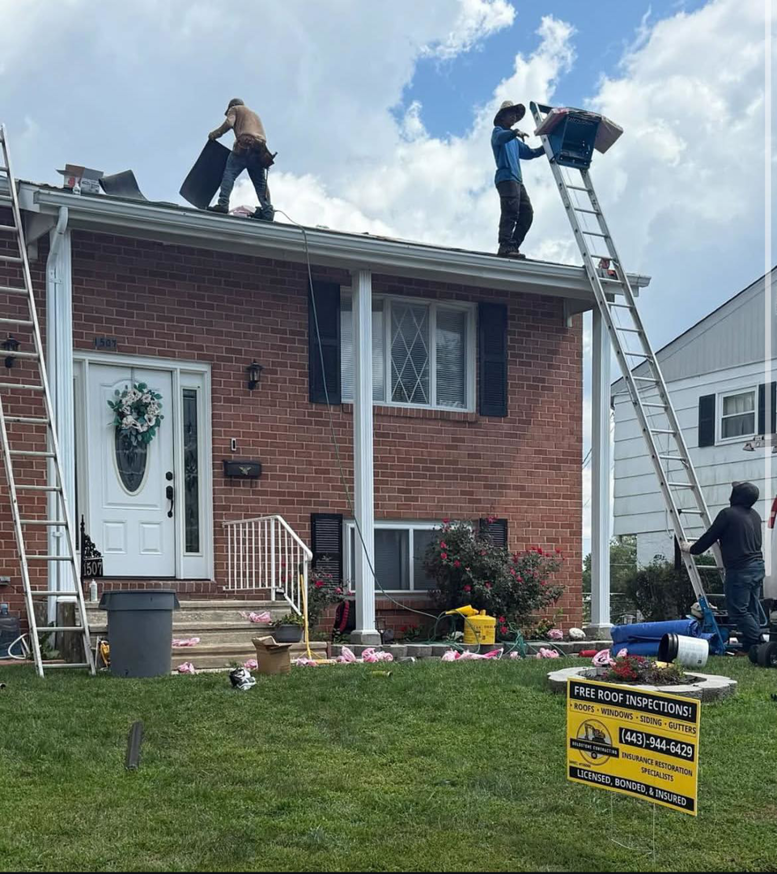 A crew working on a roof replacement project, with ladders and materials, by Goldstone Contracting Inc. in Gambrills, MD.