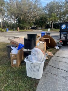 A pile of household junk, including boxes, a table, and a laundry basket, placed curbside for removal by Lightning Bay Junk Removal in Tampa, FL.