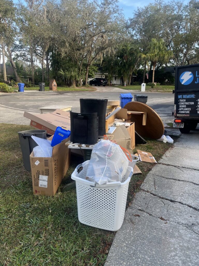 A pile of household junk, including boxes, a table, and a laundry basket, placed curbside for removal by Lightning Bay Junk Removal in Tampa, FL.