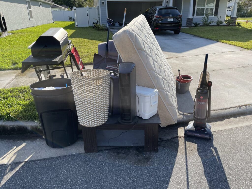 Large household items like a mattress, grill, and furniture piled curbside for junk removal by Junk Removal JAX in Jacksonville, FL.