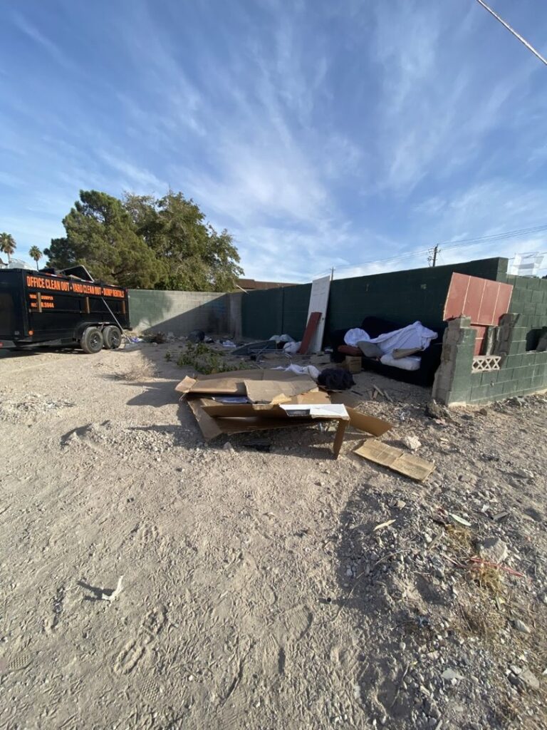 A large curbside pile of household junk, including a shopping cart and boxes, awaiting removal by Mike's Dumper in Las Vegas, NV.
