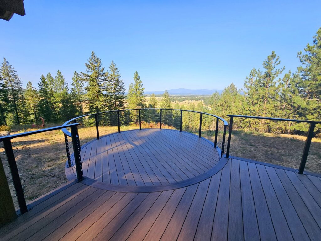A stunning curved composite deck with modern cable railing and a scenic view, designed and built by Ridgeline Decks in Spokane, WA.