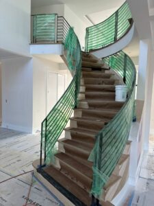 A large, curved interior staircase with metal railings covered in protective plastic during installation by Advanced Welding All in One Fabrication LLC in Guttenberg, NJ.