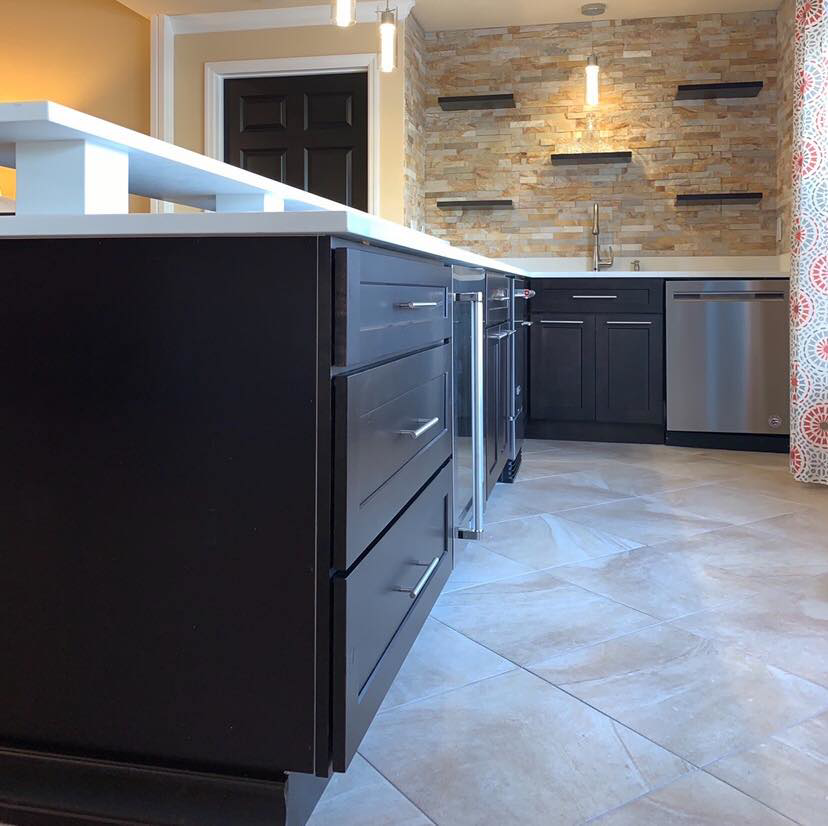 A custom-designed bar and kitchenette with dark cabinets and a stone accent wall by Catalyst Contracting in Cape Coral, FL.