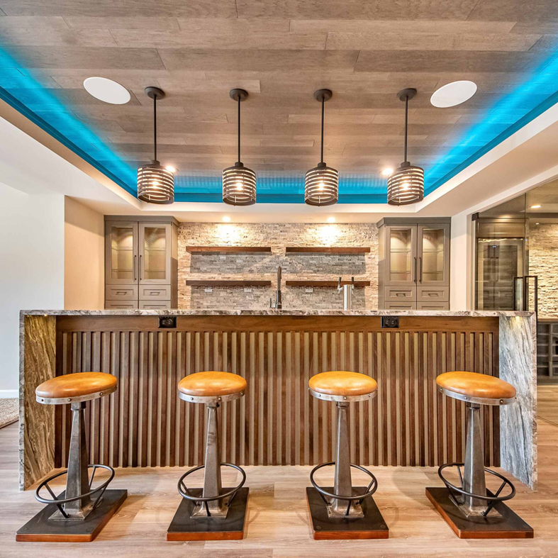 Custom basement bar design featuring pendant lights, stone backsplash, and modern cabinetry by BasementRemodeling.com in Rockville, MD.