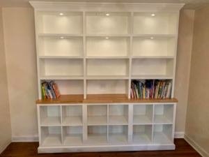 A custom-built white bookshelf and storage unit with integrated lighting by J Development in Pittsburgh, PA.