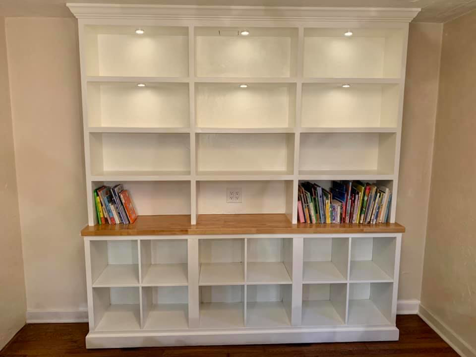 A custom-built white bookshelf and storage unit with integrated lighting by J Development in Pittsburgh, PA.