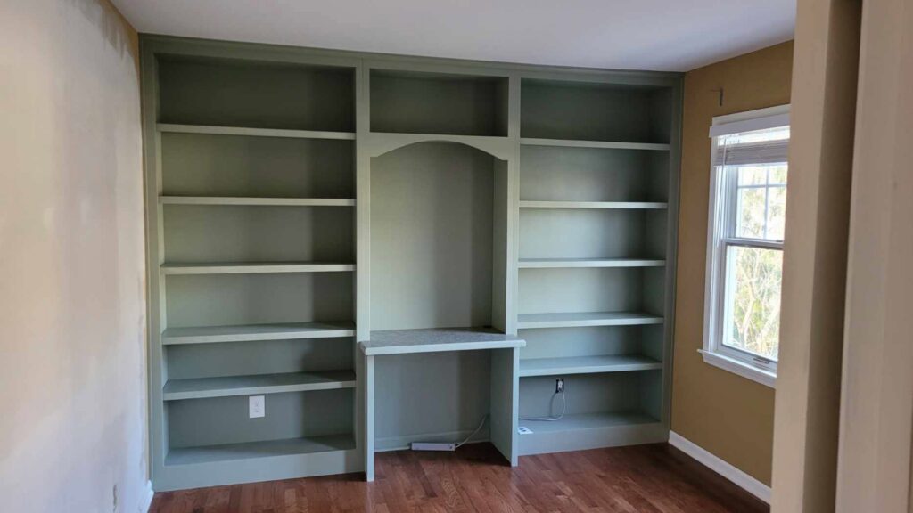 Custom built-in bookshelves with an integrated desk area, painted green, installed by CLE Remodeling Co in Cleveland, OH.