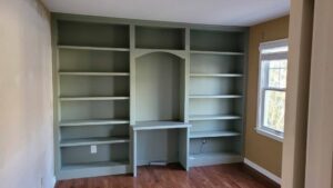 Custom built-in bookshelves with an integrated desk area, painted green, installed by CLE Remodeling Co in Cleveland, OH.