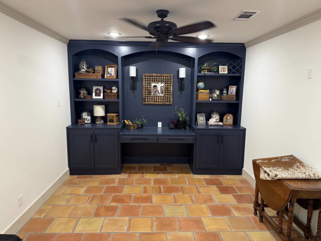 A custom-built desk and shelving unit with dark blue cabinetry in a room with terracotta floor tiles, completed by Javier's Painting in San Angelo, TX.
