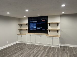 A custom built-in media center with a mounted TV, floating shelves, and white cabinets by Inspired Renovation & Hardscape's in Lorain, OH.
