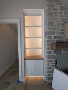 Custom built-in shelving unit with lighting next to a stone fireplace by Roche Painting in Allentown, PA.