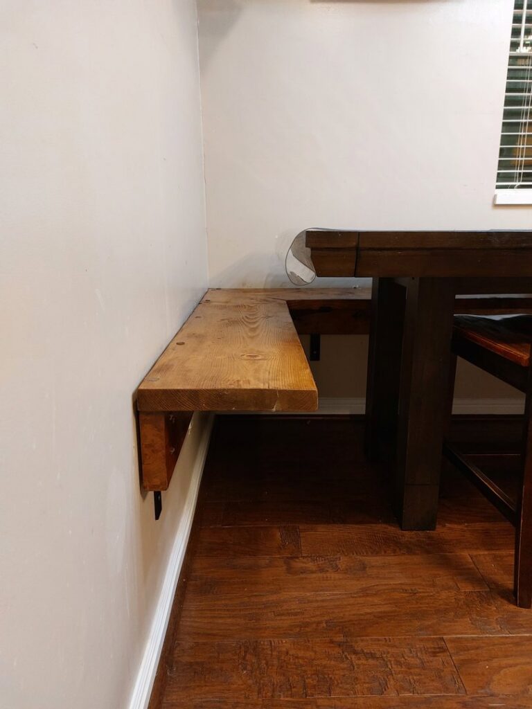 A custom-built wooden bench securely attached to a wall next to a dining table, crafted by Jake and Jake Construction LLC in Sandy, UT.