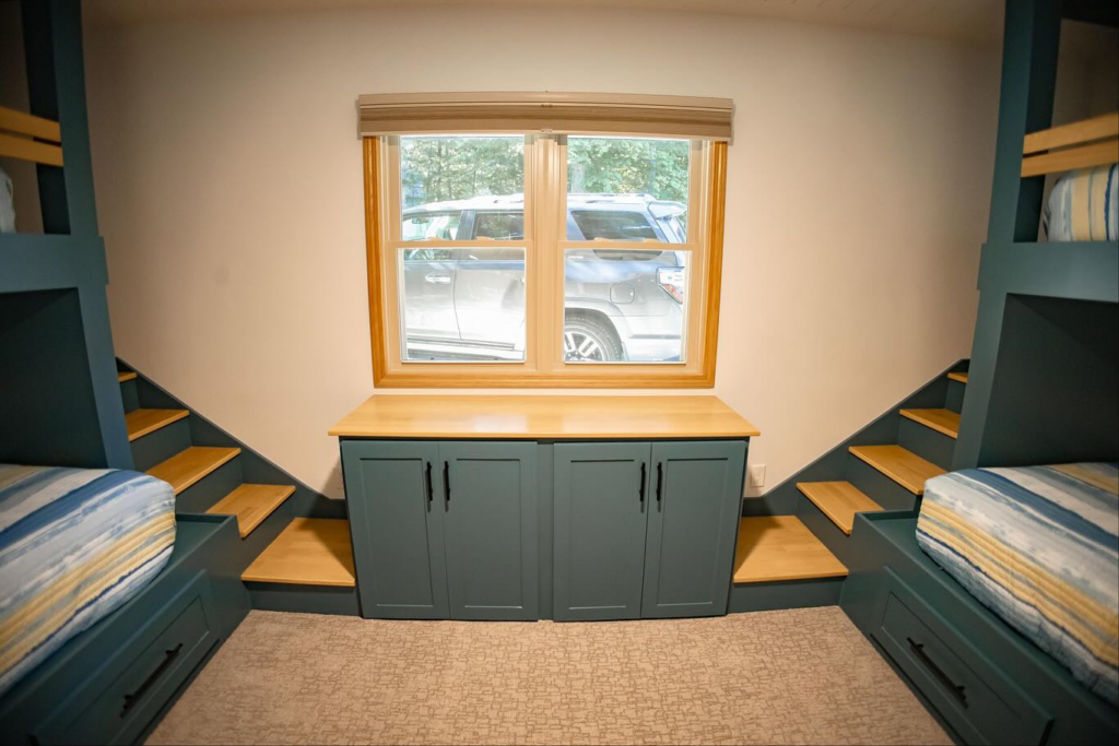 Custom built bunk beds with integrated stairs and storage cabinets under a window by An Extra Hand in Indianapolis, IN.