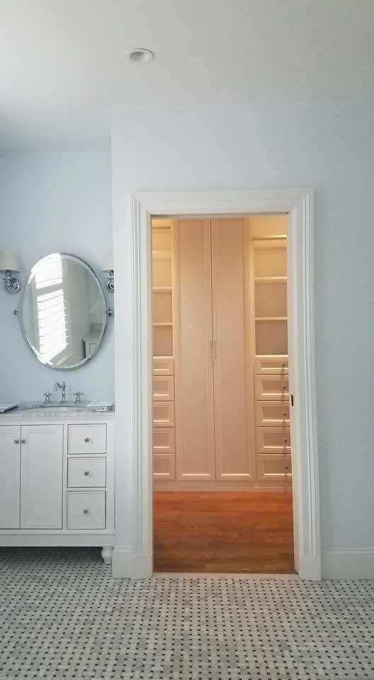A custom walk-in closet with built-in shelving visible from a bathroom with a white vanity by Caldwell Construction in Richardson, TX