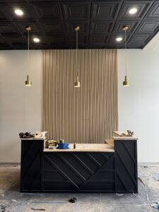 A custom-built commercial reception desk with wood slat wall paneling by Benjamin Design - Build in Fishers, IN.