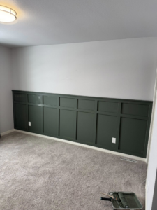 A newly installed dark green wainscoting accent wall with painting tools on the floor by LIV Custom Accents in West Fargo, ND