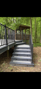 A custom-built deck with stairs and railings leading to a small gazebo in a wooded area by Nader Builders in Ann Arbor, MI.