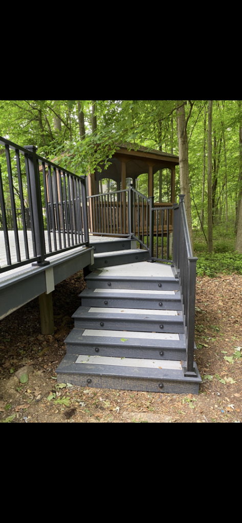 A custom-built deck with stairs and railings leading to a small gazebo in a wooded area by Nader Builders in Ann Arbor, MI.