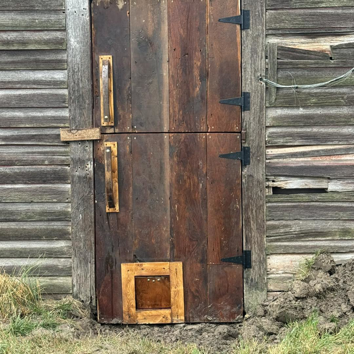 A custom rustic wooden double door with a small access opening at the bottom by Shurigar Home Repair & Handyman in Kenesaw, NE.