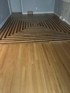 A unique geometric pattern hardwood floor design installed by Nelson Hardwood Flooring in Madison, WI, transitioning to standard planks.