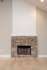 A custom home fireplace with a brick surround and shiplap accent wall by Aubrey Homes in Austin, TX