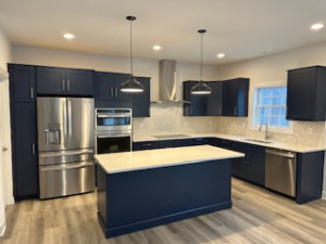 A custom kitchen design with dark blue cabinets, a matching island, and stainless steel appliances by McDonald Custom Homes in Schenectady, NY.