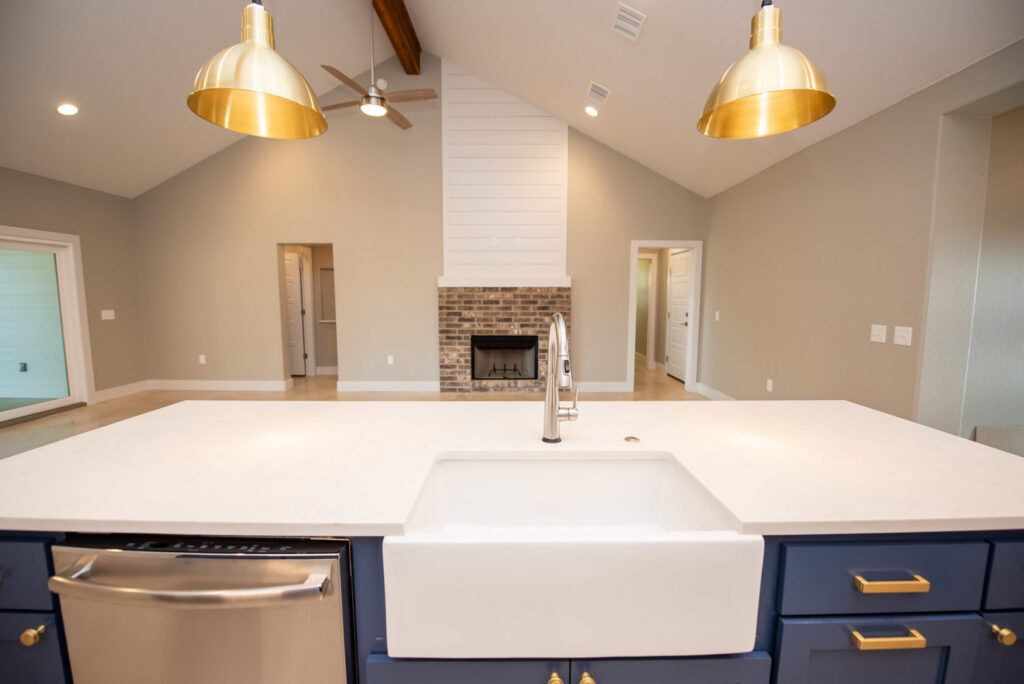 A custom kitchen island with a farmhouse sink, overlooking a living room with a fireplace by Aubrey Homes in Austin, TX