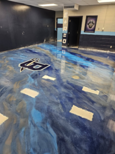 A custom 'P' logo integrated into a blue and gold epoxy floor by New Age Decorative Concrete in Broussard, LA.